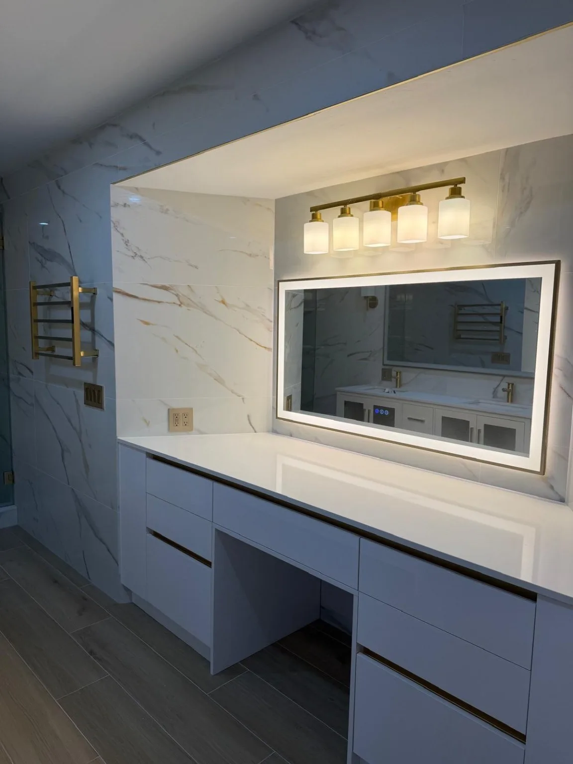 Bathroom vanity with white cabinetry, LED-lit mirror and marble-look tile walls