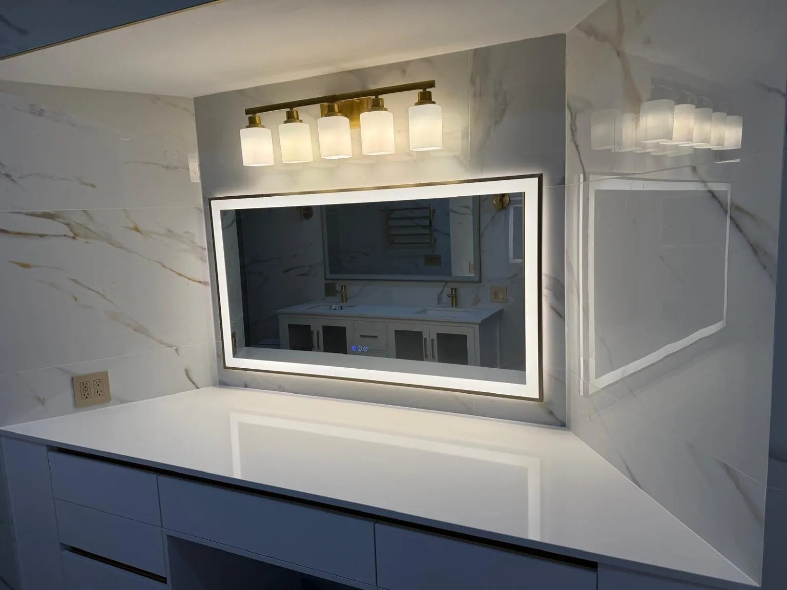 Bathroom vanity detail with LED-lit mirror, gold fixtures and marble-look tile