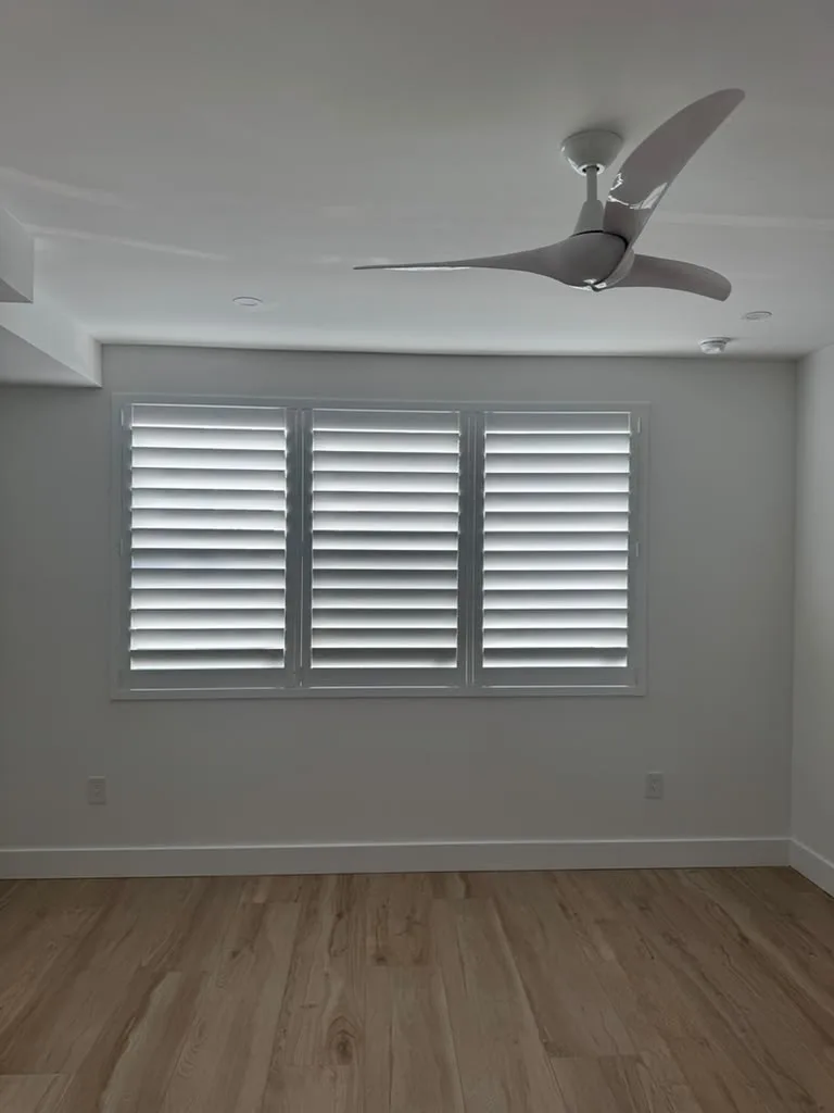 White plantation shutters installed across a Miami bedroom window wall by JT Express Solutions